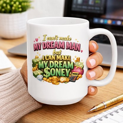 White ceramic coffee mug with a funny dating and money quote, “I can’t make my dream man, but I can make my dream money,” shown in a cozy desk workspace.